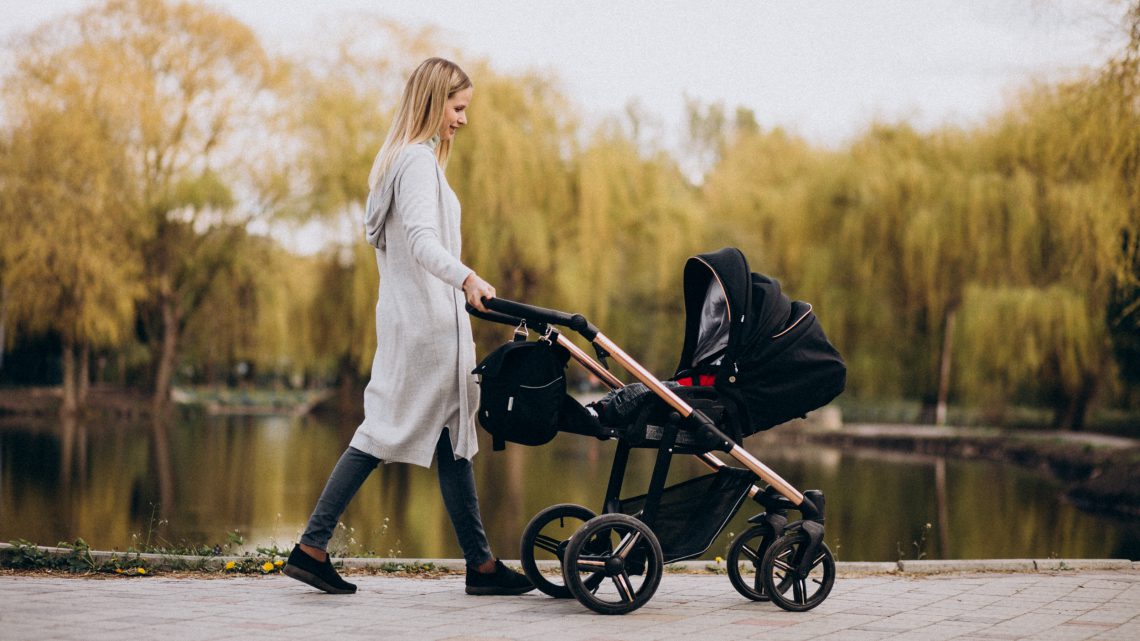 Polskie wózki dziecięce - młoda mama na spacerze w parku z dzieckiem w wózku w jesienny dzień