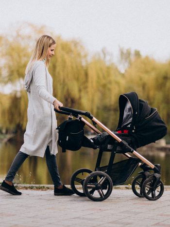 Polskie wózki dziecięce - młoda mama na spacerze w parku z dzieckiem w wózku w jesienny dzień