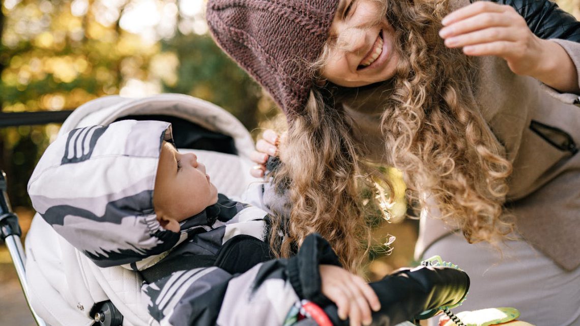 dziecko w wózku spacerowym z gondolą bawiące się włosami matki