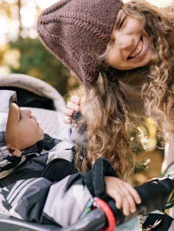 dziecko w wózku spacerowym z gondolą bawiące się włosami matki