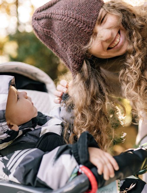 dziecko w wózku spacerowym z gondolą bawiące się włosami matki