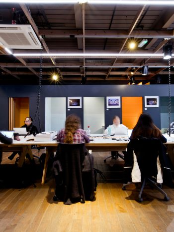 Grupa osób siedzi przy długim stole w nowoczesnym wnętrzu i pracuje przy laptopach