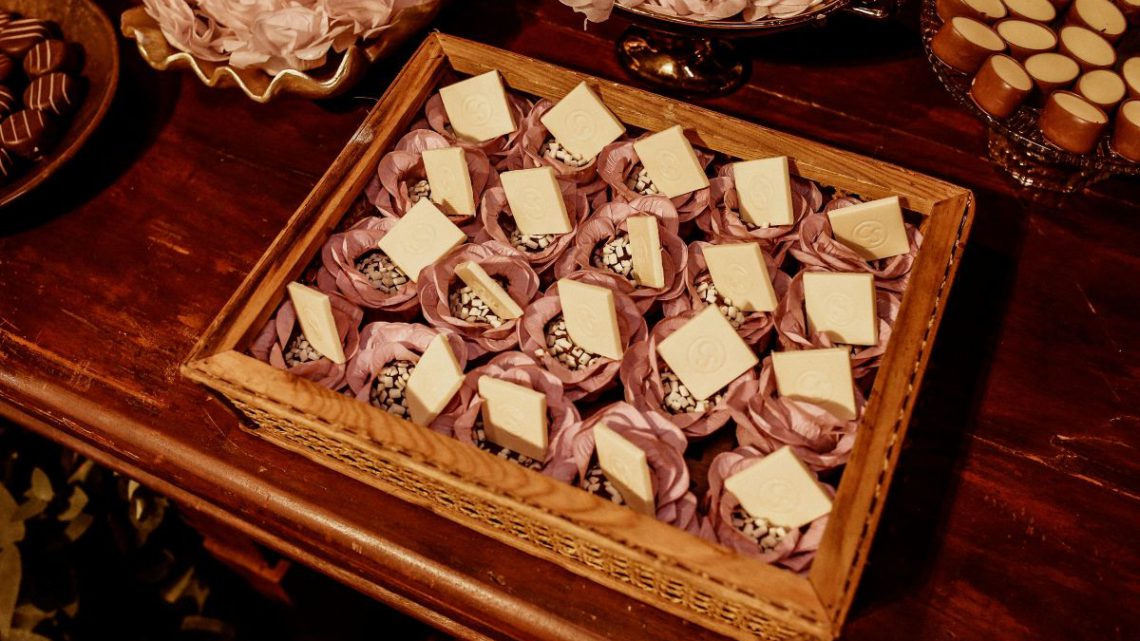 Eleganckie słodycze na święta w ozdobnych papierowych papilotkach przypominających kwiaty, ułożone w drewnianej tacy na stole.