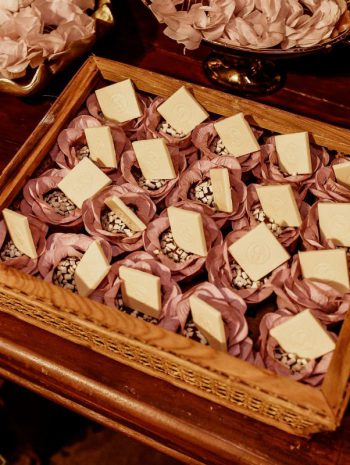 Eleganckie słodycze na święta w ozdobnych papierowych papilotkach przypominających kwiaty, ułożone w drewnianej tacy na stole.